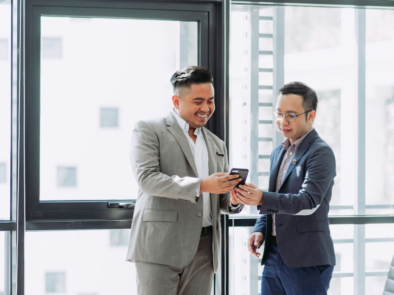 Deux hommes en costume d'affaires qui sourient en regardant un appareil mobile